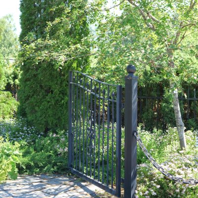 Puutarhassa kivetyksiä, musta rautainen portti sekä mustat paksut ketjut rajaavat puutarha-aluettaa.
